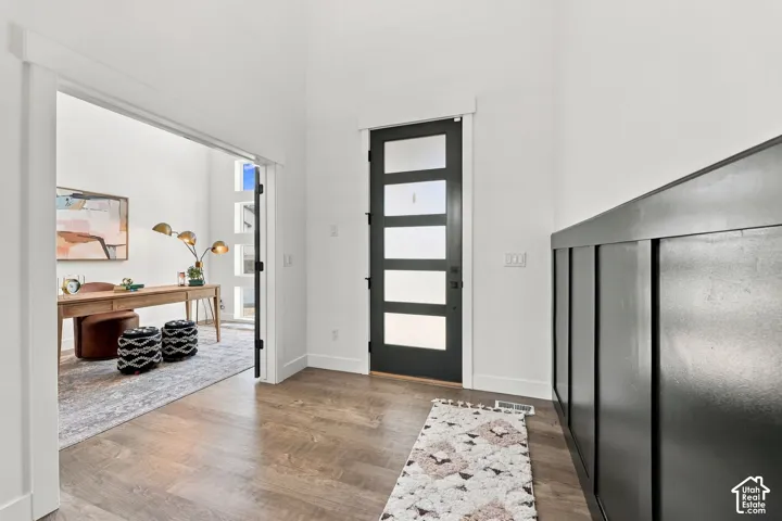 Wood-finish flooring with white baseboards, modern black front door with frosted glass panels, and dark wainscoting paneling