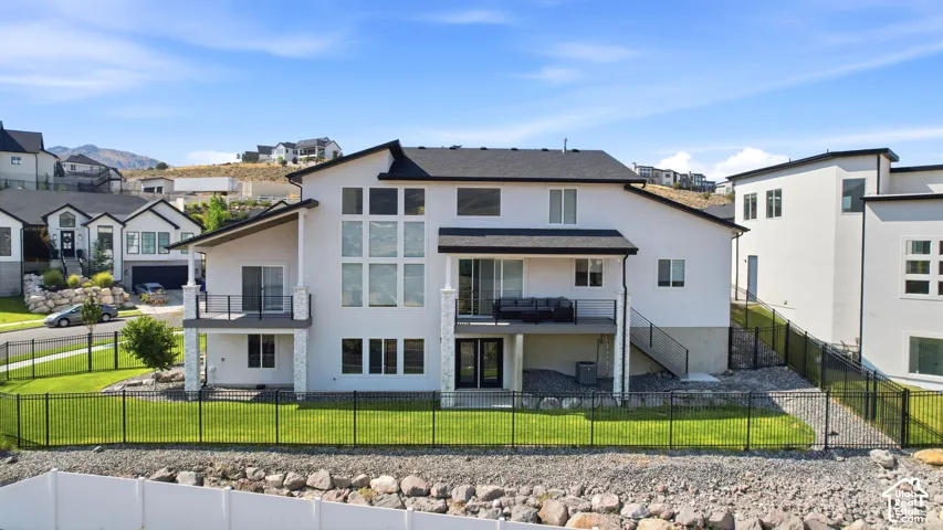 Contemporary multi-story residence featuring a white stucco exterior with black trim, multiple balconies, a lower-level patio, and extensive fenestration