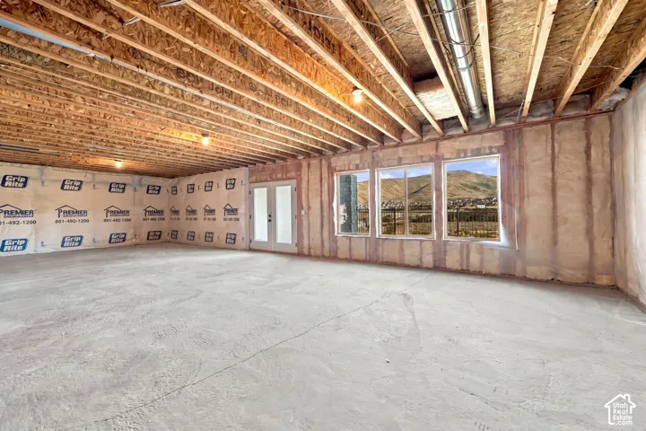 Unfinished basement space with exposed wood joists, concrete flooring, three windows, and a double-door entry