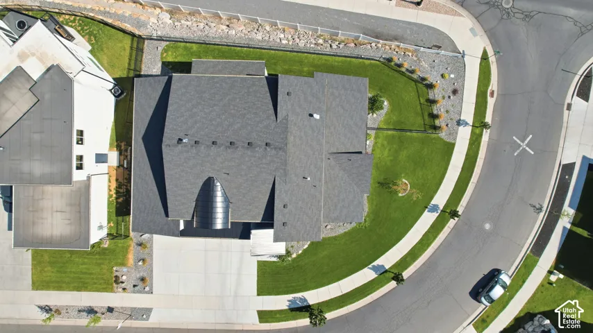 Lush green lawn with mature landscaping, asphalt shingle roof, and curved driveway