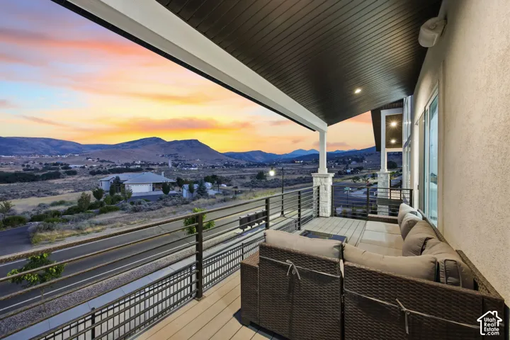 Expansive covered balcony featuring a composite deck, metal railing, stone columns, and recessed lighting