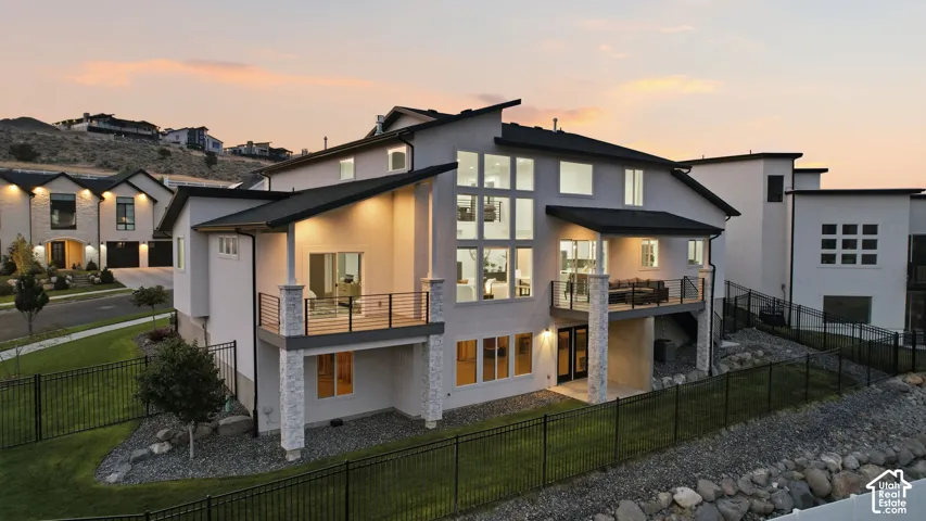 Contemporary architectural design featuring expansive windows, multiple elevated balconies with metal railings, a stone-accented lower level, and a fenced backyard