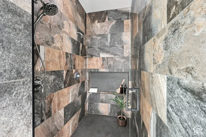 Walk-in shower with full-height stone-look tile, built-in shelving, glass shower door, and a multi-function showerhead
