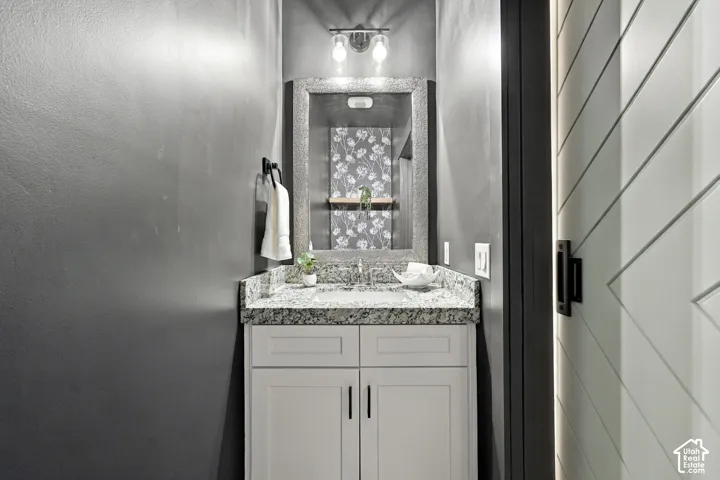 White shaker-style vanity with a granite countertop, undermount sink, and black hardware