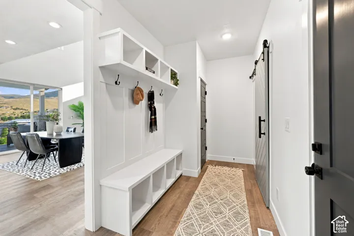 Built-in storage bench with upper shelving and coat hooks, wood-finish flooring, recessed lighting, and a sliding barn door