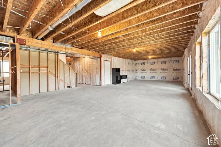 Unfinished basement featuring exposed wood joists, concrete flooring, multiple windows, and a framed-in staircase