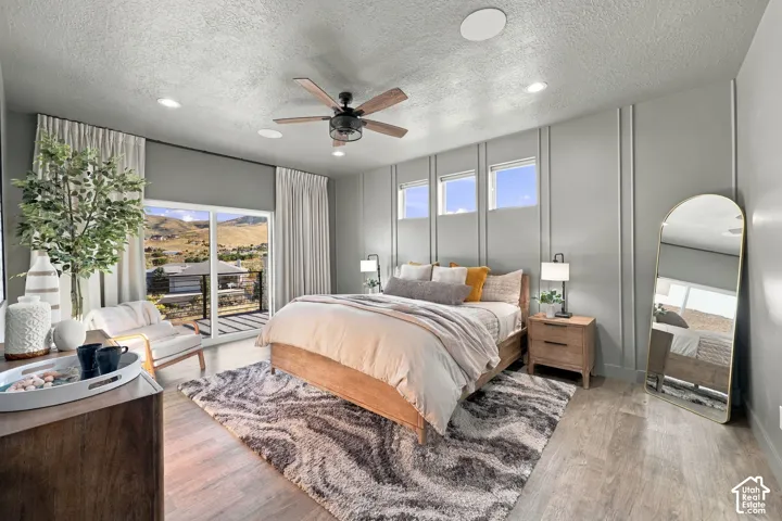 Wood-finish flooring, recessed lighting, ceiling fan with integrated light, accent wall with vertical paneling, and sliding glass door leading to a balcony