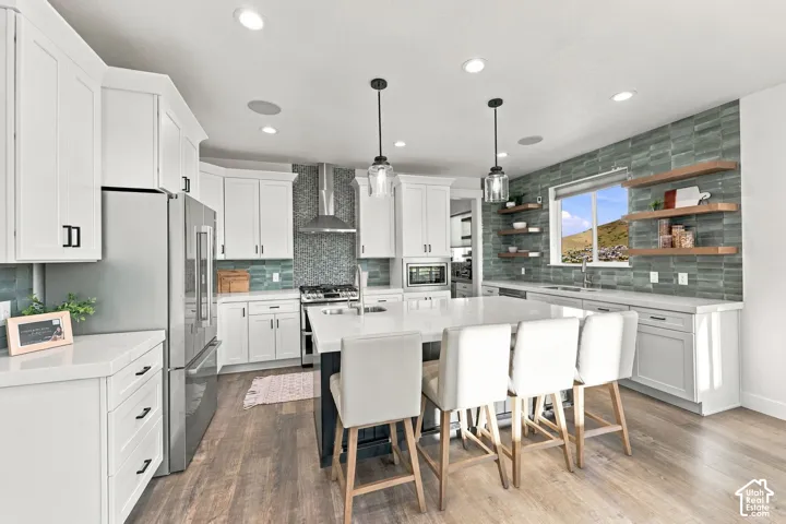 Gourmet kitchen featuring white shaker cabinetry, stainless steel appliances, a large center island with seating, pendant lighting, and wood-finish flooring
