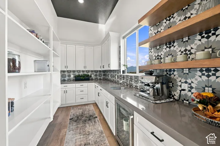 White cabinetry with contrasting dark hardware, extensive pantry shelving, patterned tile backsplash, wood-finish open shelving, and a built-in beverage refrigerator