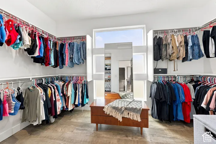 Expansive closet featuring wood-finish flooring, a built-in window, and multiple clothing rods