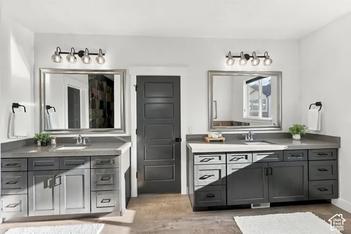 Dual vanities with integrated sinks, dark wood-finish cabinetry, light stone countertops, and individual framed mirrors with integrated lighting