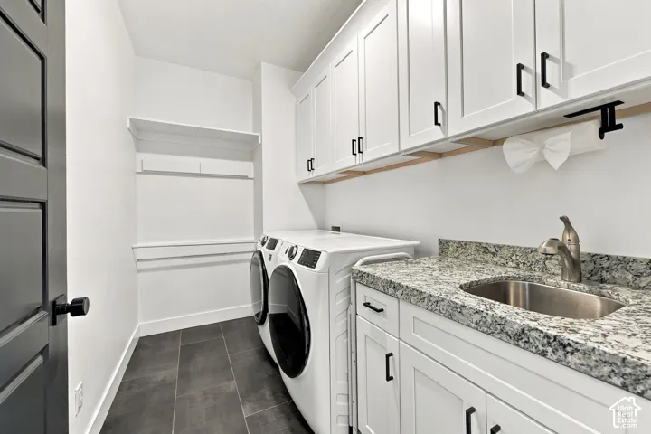 White shaker cabinetry with black hardware, stone-finish countertop with undermount sink, and dark rectangular floor tiling