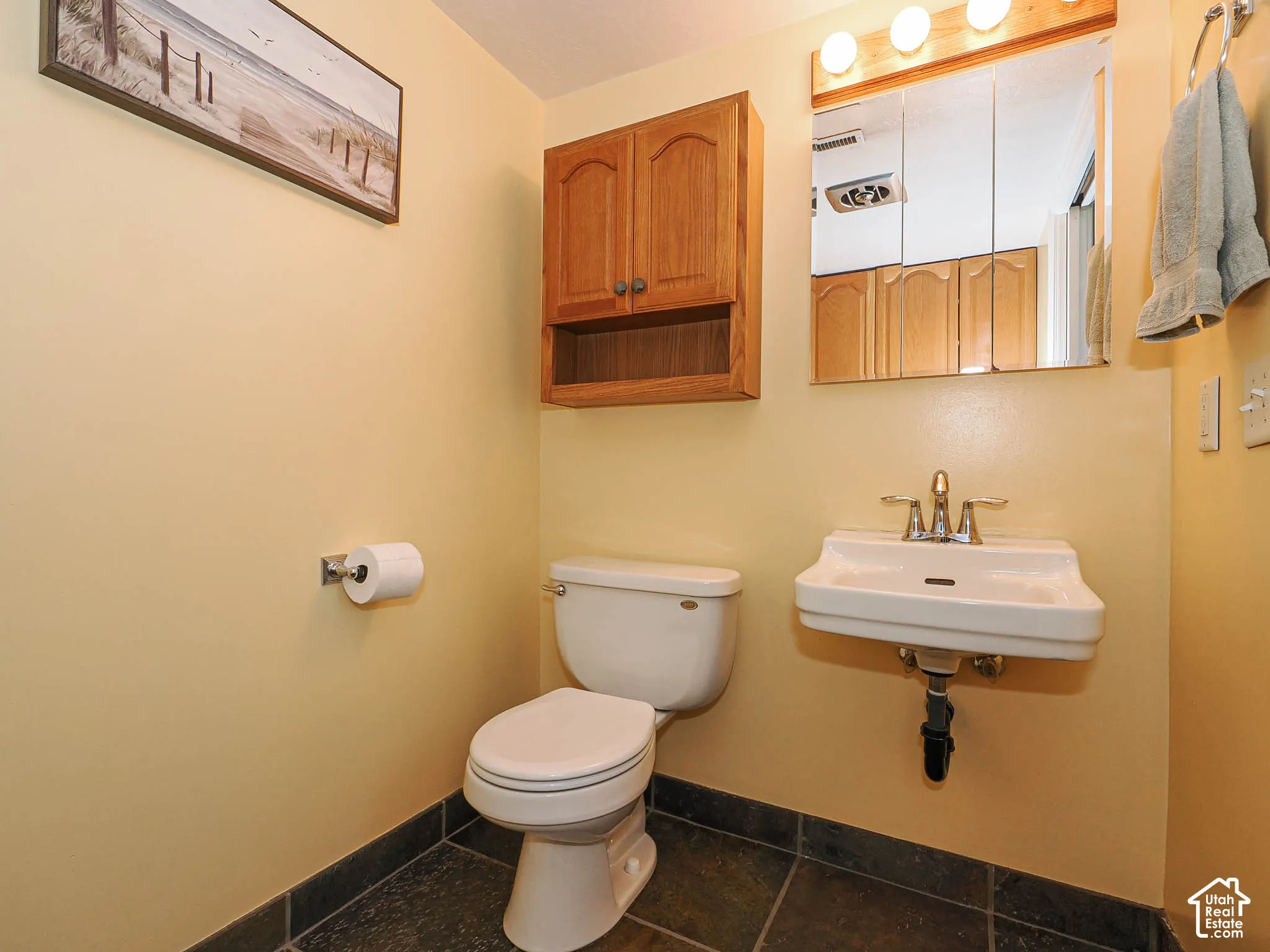 Wall-mounted sink with chrome faucet, medicine cabinet with integrated lighting, and a wall-mounted wooden cabinet