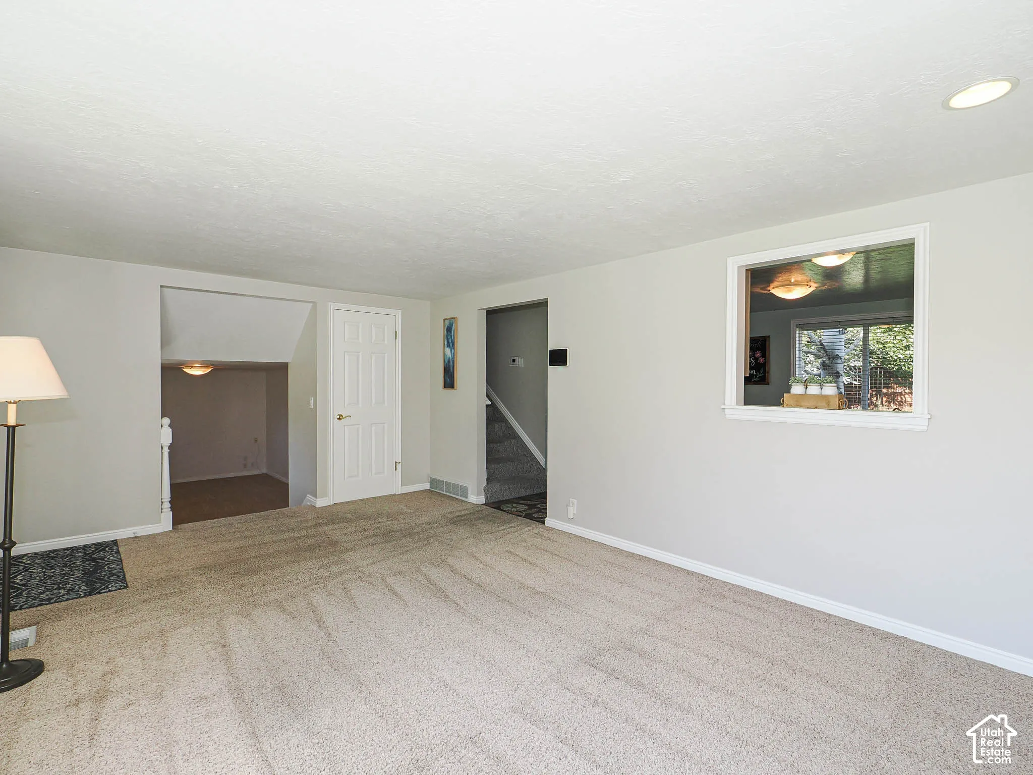 Recessed lighting and a white trim window complement the light-colored walls and carpeted flooring