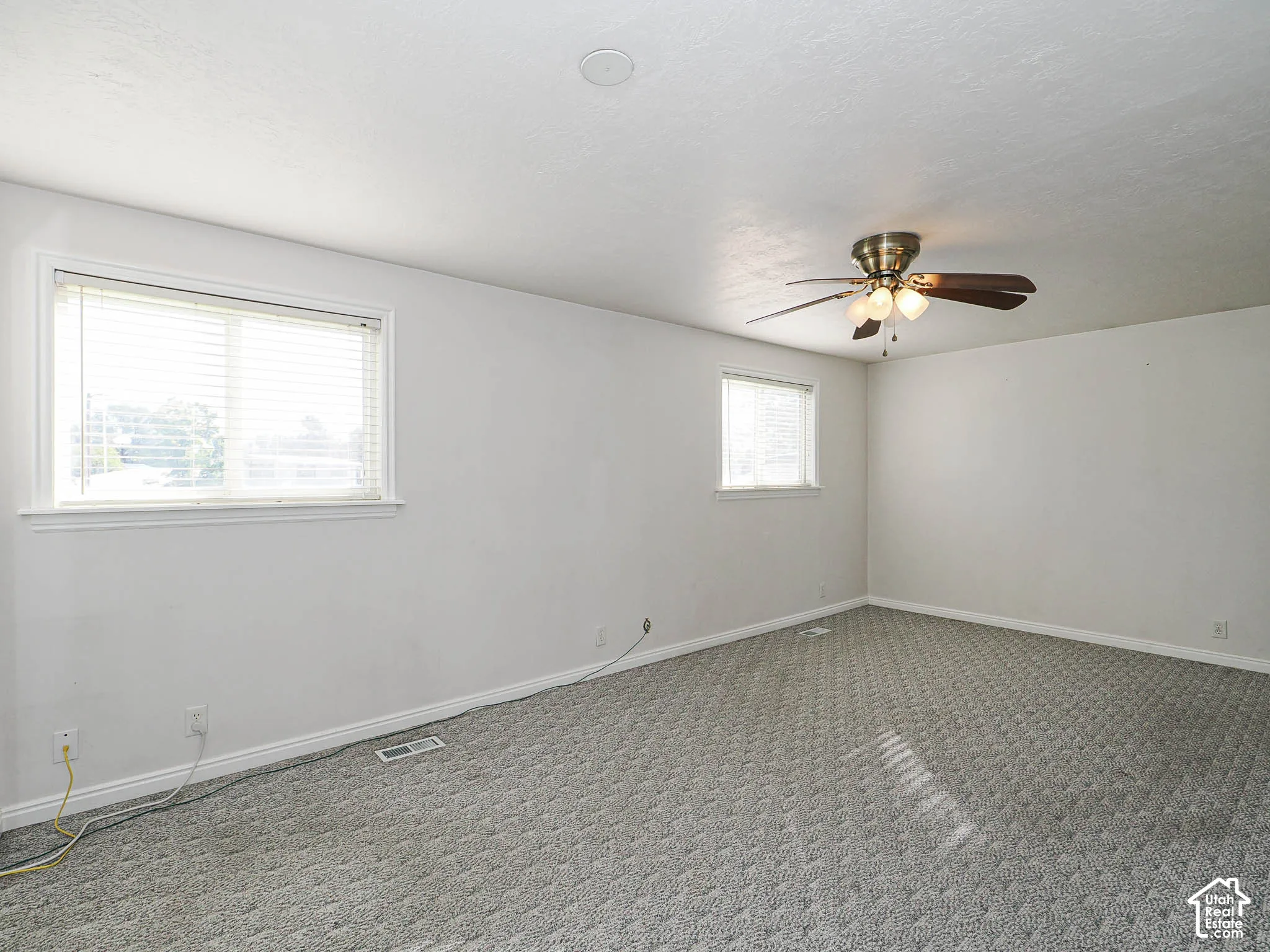 Recessed ceiling lighting, ceiling fan with integrated light fixture, two windows with blinds, and neutral carpeting