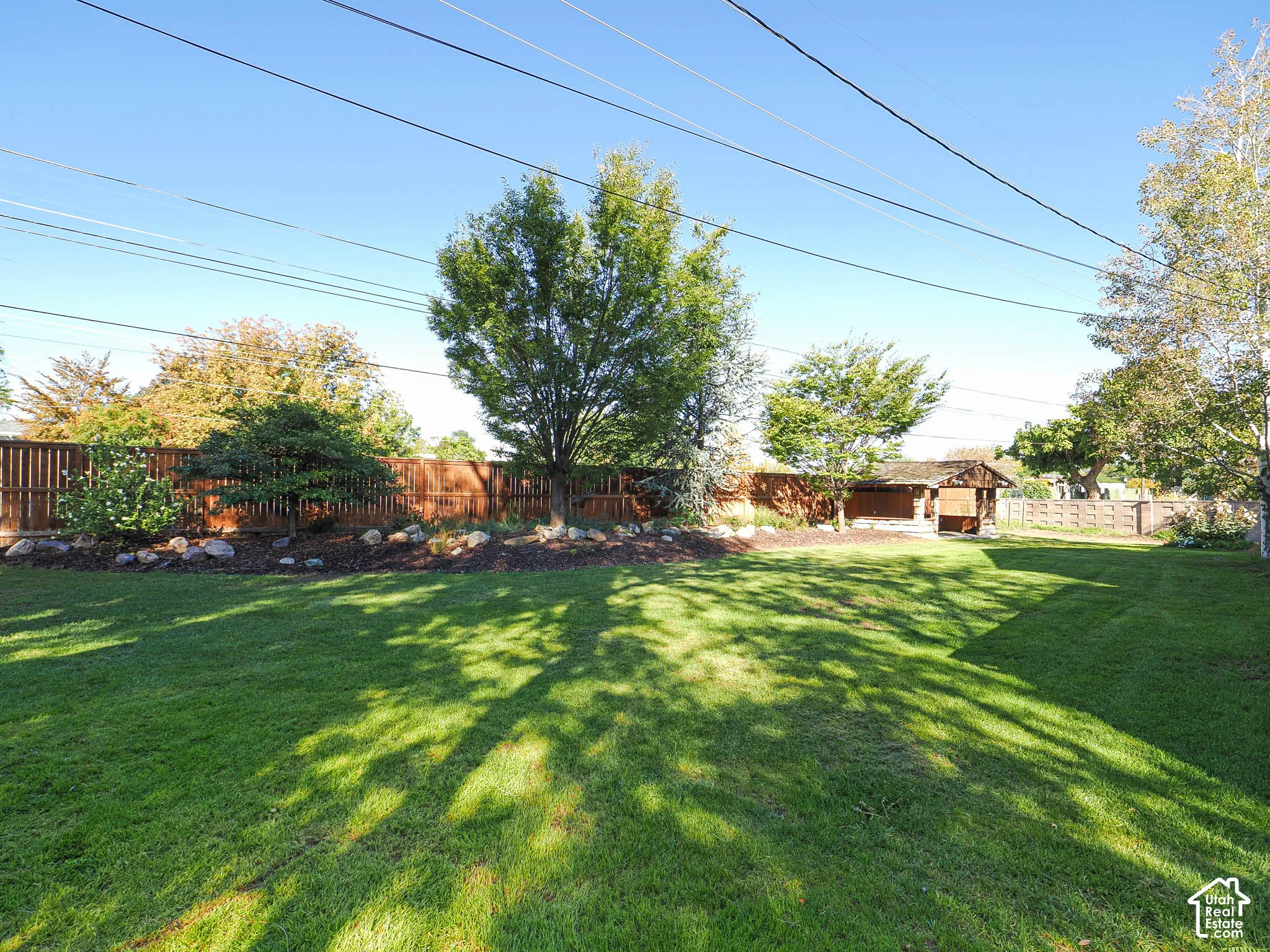 Expansive grassy yard with a wooden privacy fence, mature trees, and a dedicated garden bed