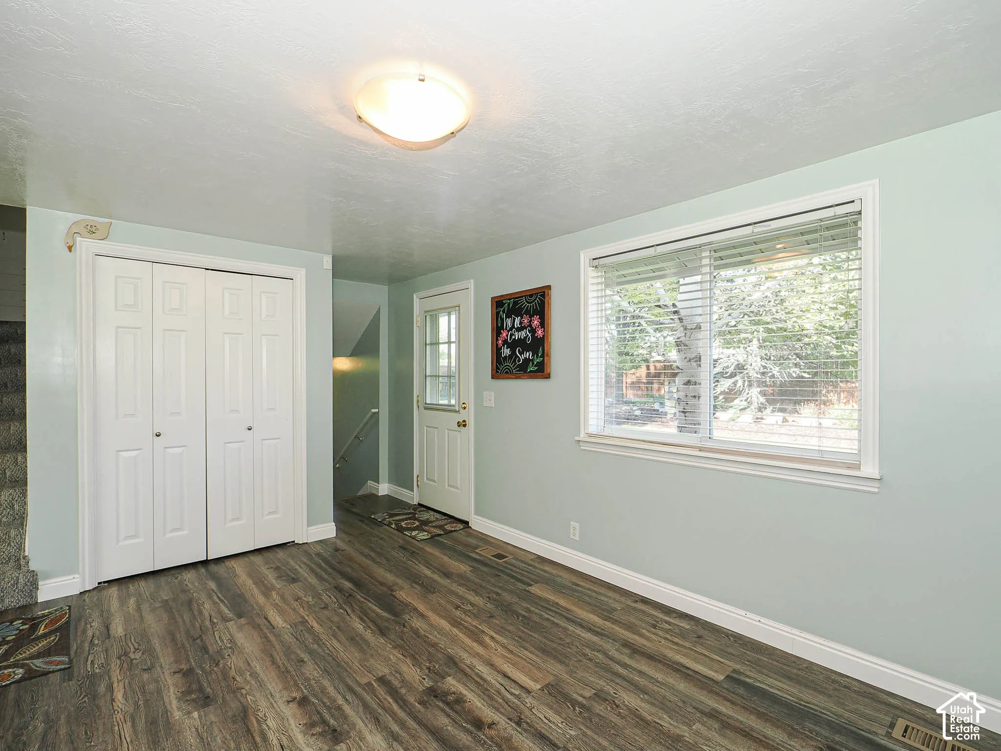 Wood-finish flooring, white bi-fold closet doors, contemporary flush mount light fixture, window with blinds, and a white exterior door with glass insert
