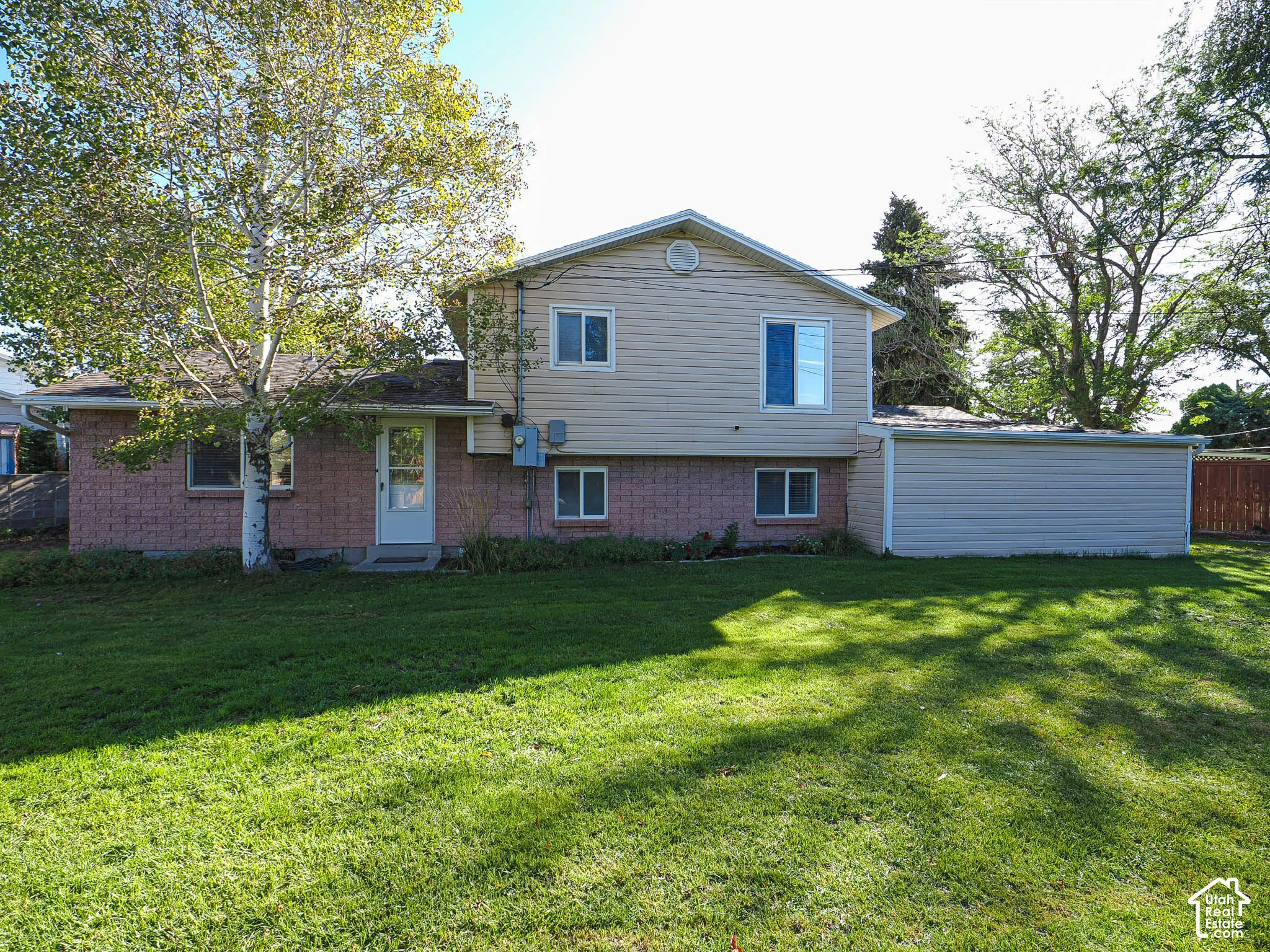 Expansive green lawn with mature trees and a two-story residence featuring brick and siding exterior finishes