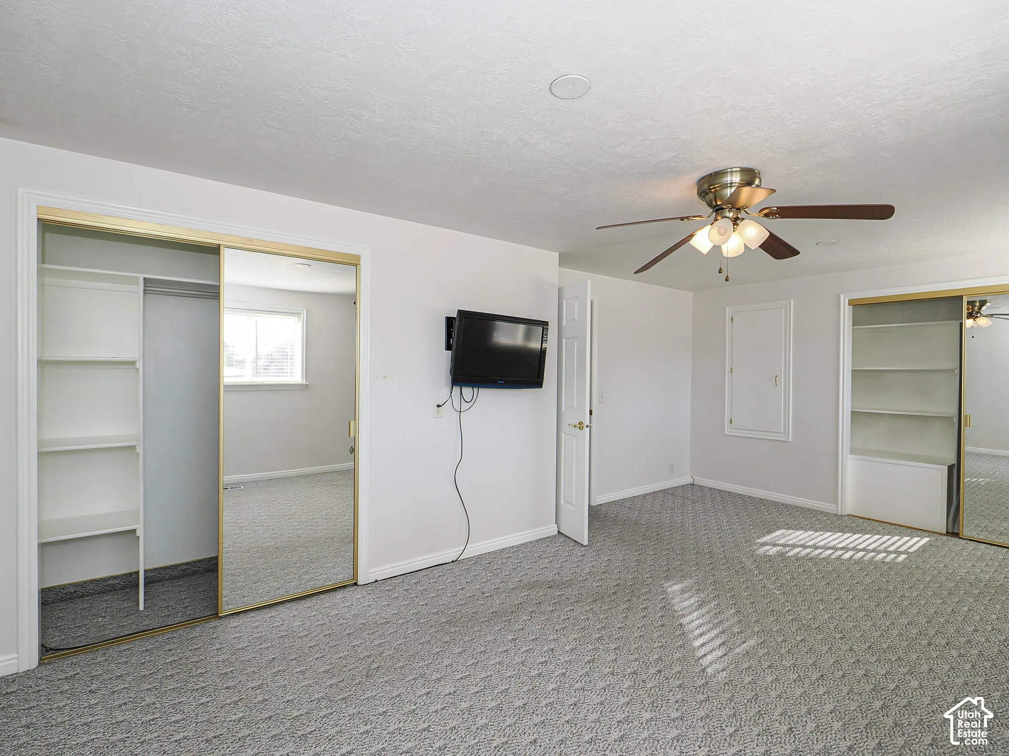 Mirrored sliding closet doors with built-in shelving, textured carpet flooring, and a ceiling fan with integrated lighting