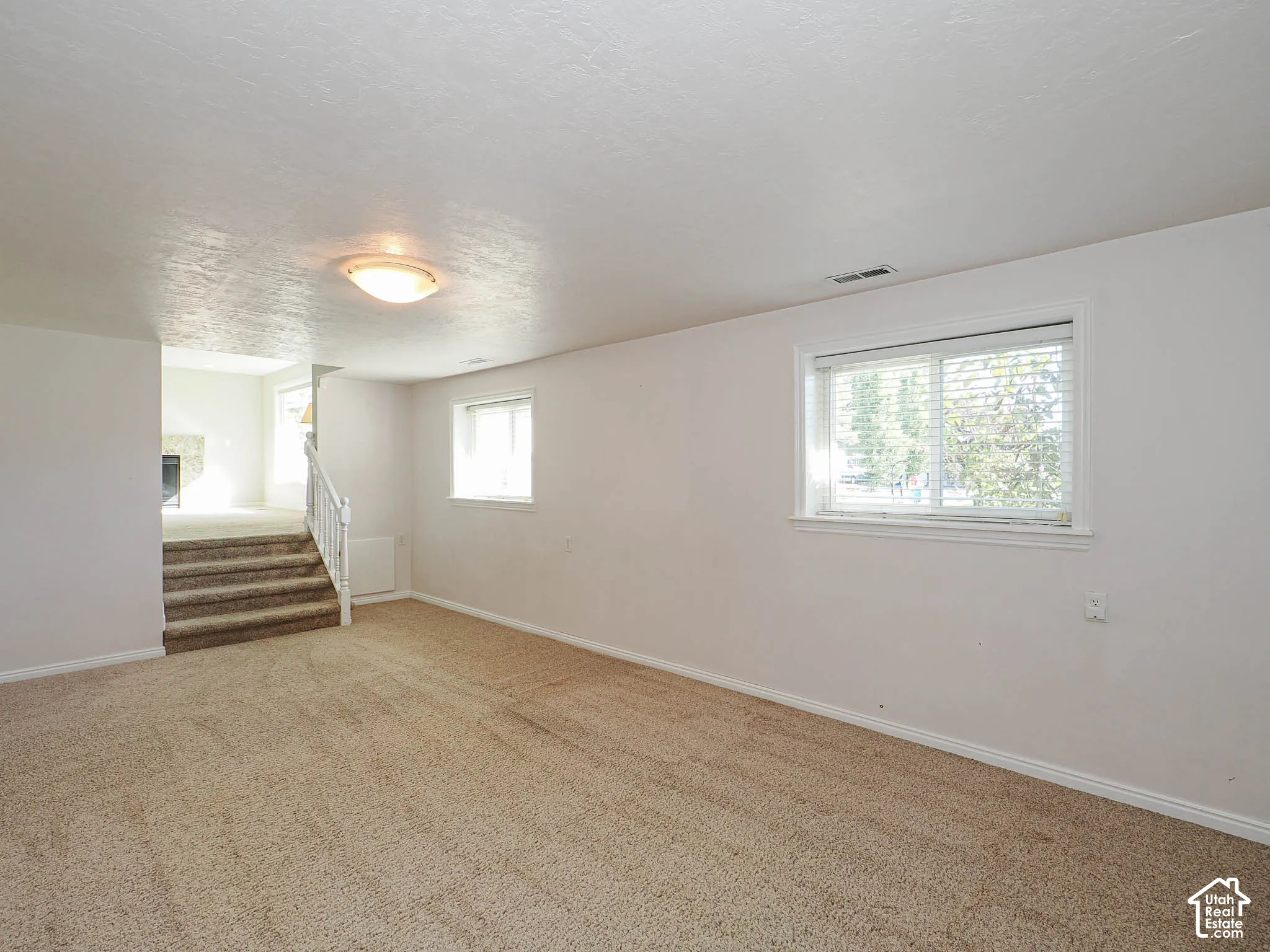 Carpeted room with multiple windows, an overhead light fixture, and a carpeted staircase with white railings