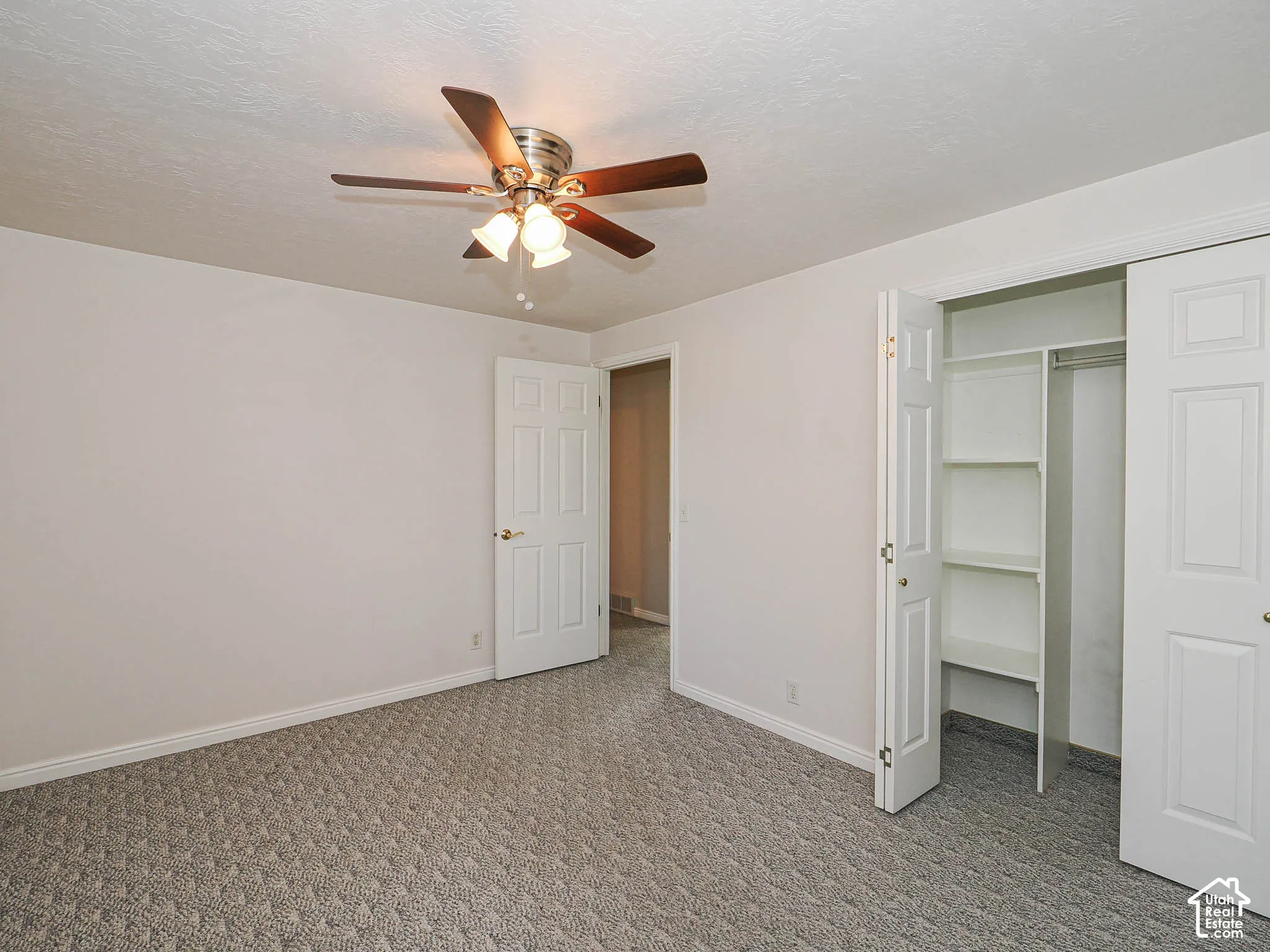 Textured carpet flooring, ceiling fan with integrated lighting, paneled interior doors, and built-in closet shelving
