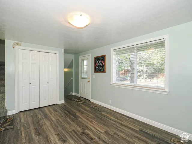 Wood-finish flooring, white bi-fold closet doors, contemporary flush mount light fixture, window with blinds, and a white exterior door with glass insert