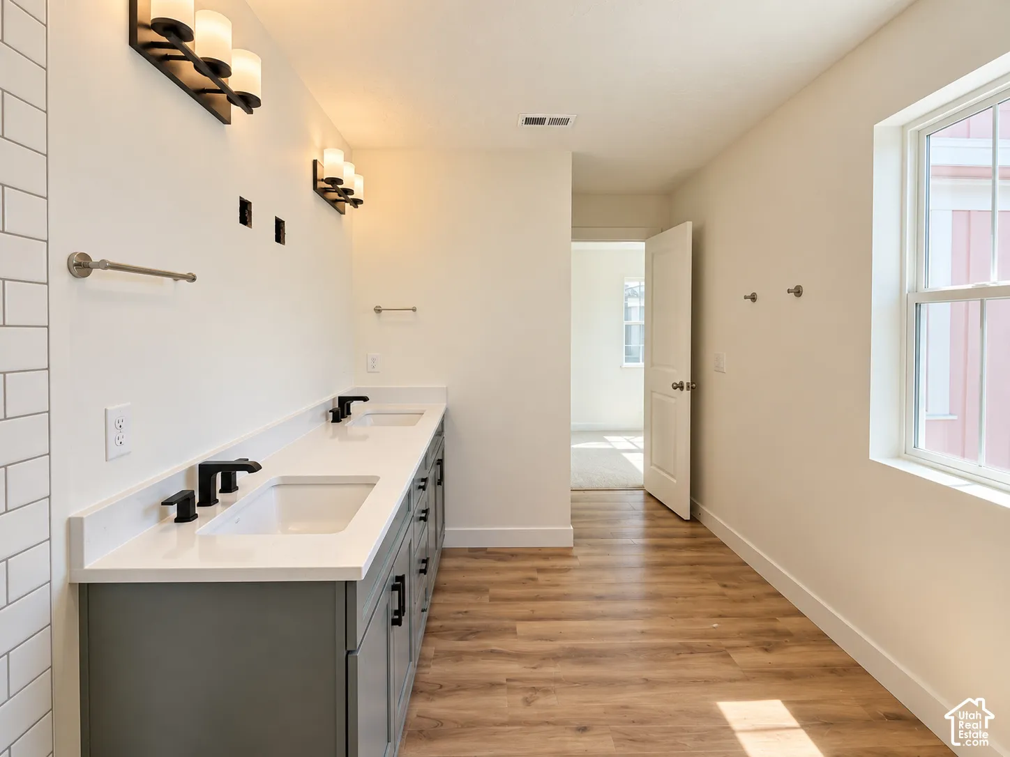 Double vanity with undermount sinks, wood-finish flooring, and a large window