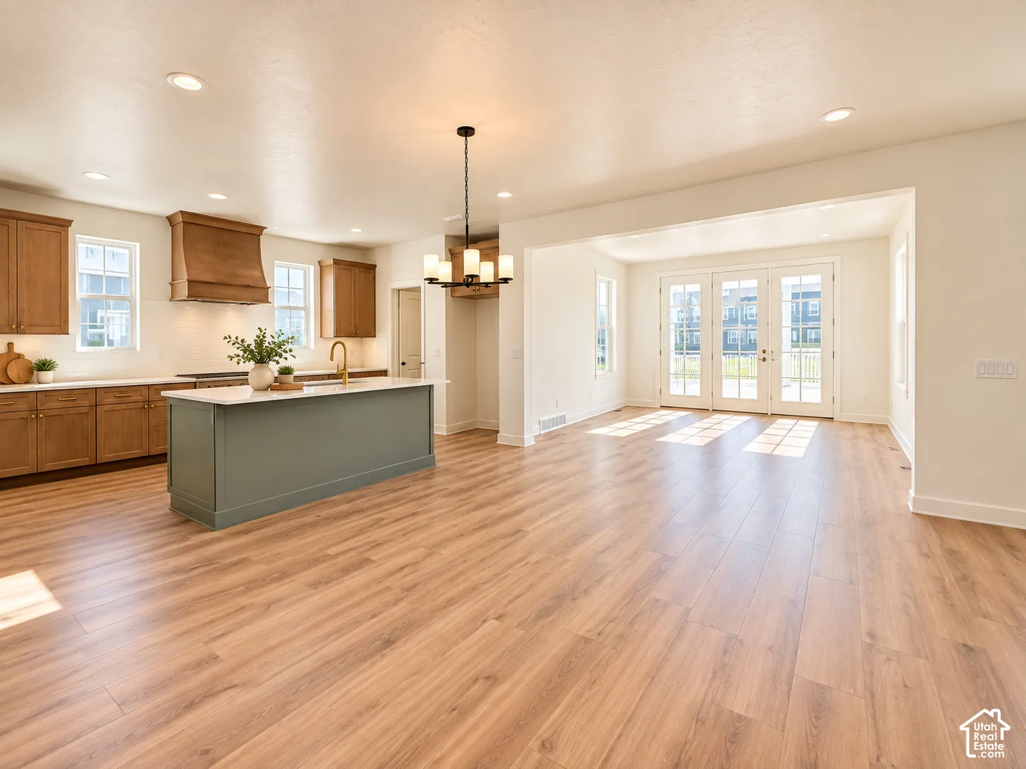 Open-concept living space with wood-finish flooring, a kitchen island with a light-colored countertop, and a kitchen featuring a wood range hood