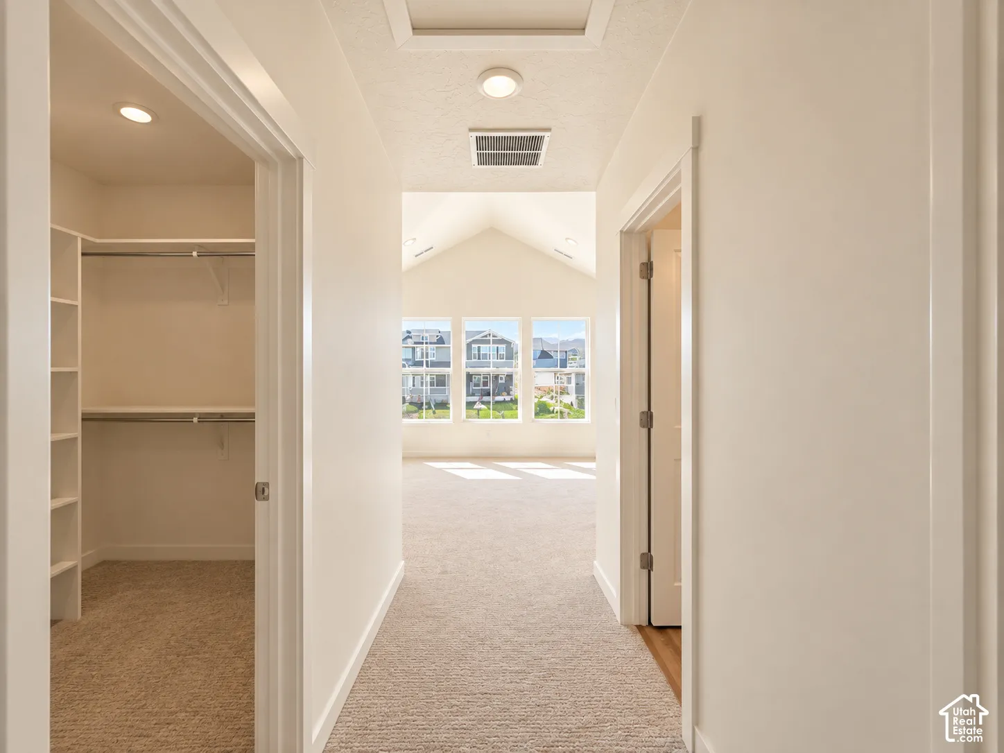 Hallway with recessed lighting and neutral carpet flooring, leading to a room with multiple windows and a vaulted ceiling