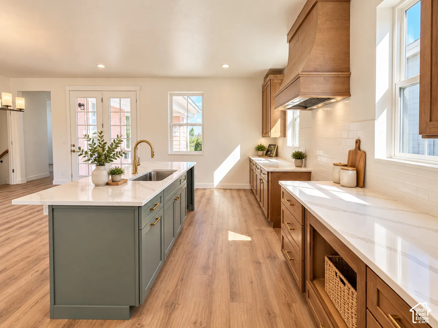 Kitchen featuring wood-finish flooring, a center island with a double basin sink, white countertops, built-in cabinetry, and a wood range hood