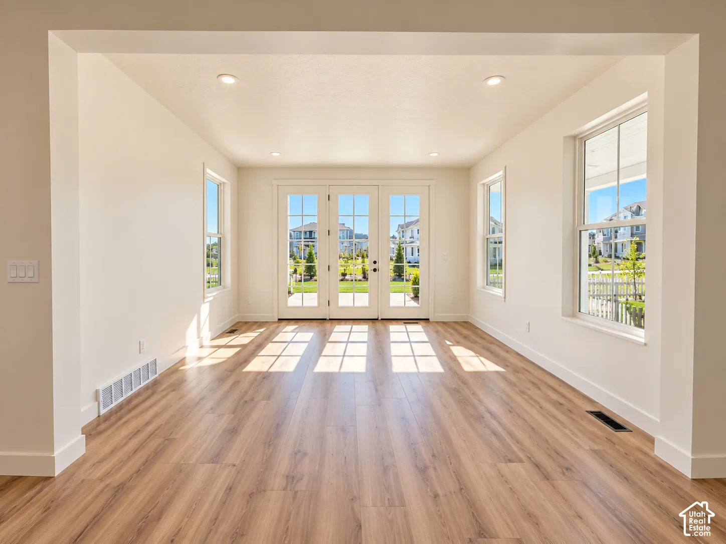 Wood-finish flooring, recessed ceiling lighting, multiple windows, and a set of French doors