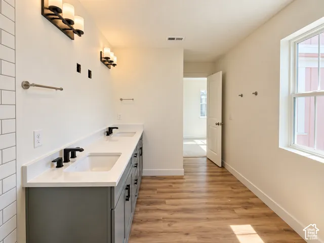 Double vanity with undermount sinks, wood-finish flooring, and a large window