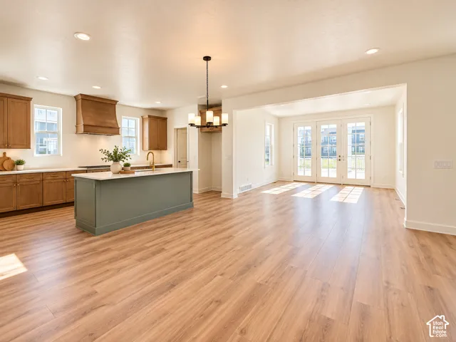Open-concept living space with wood-finish flooring, a kitchen island with a light-colored countertop, and a kitchen featuring a wood range hood
