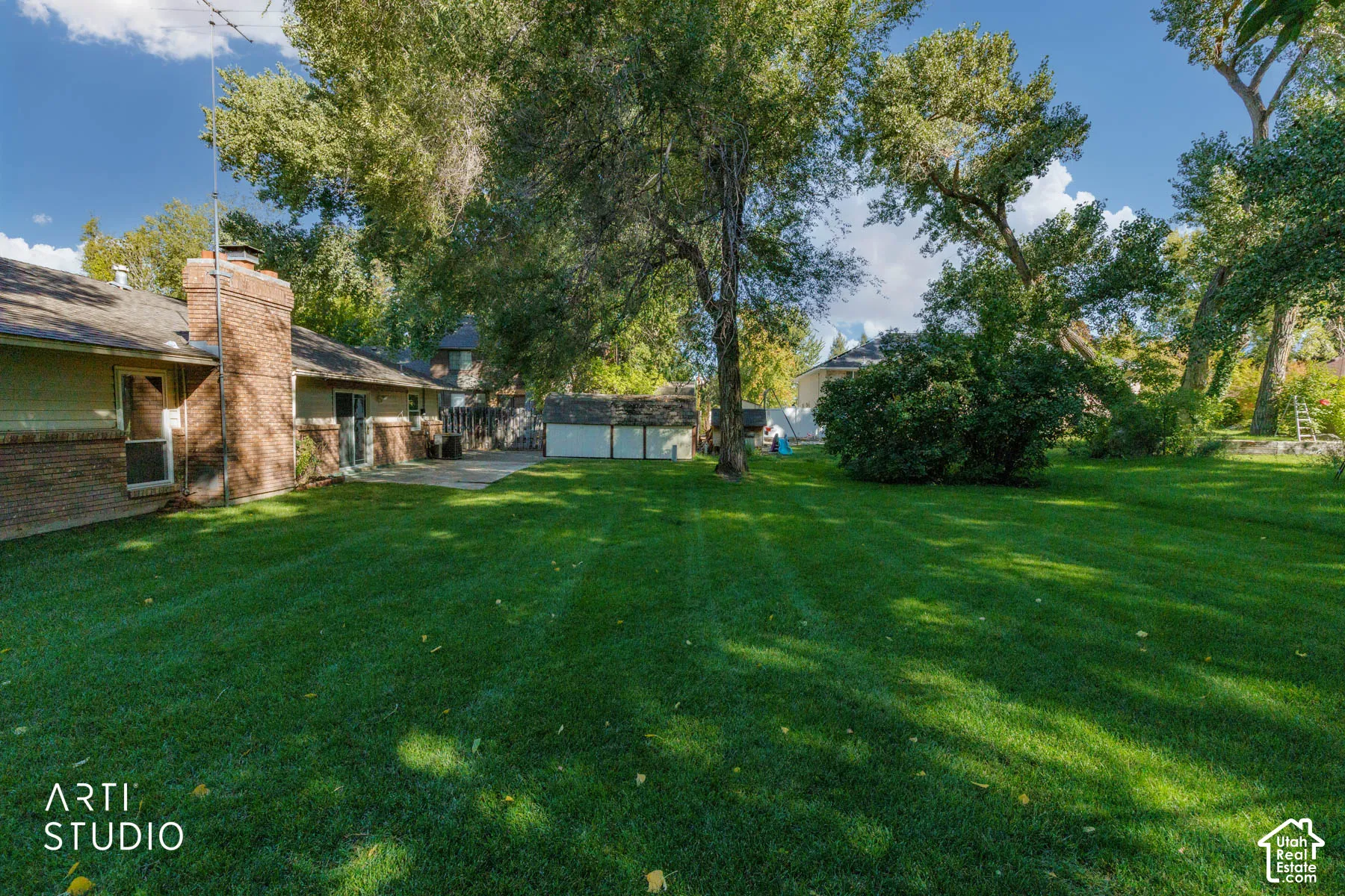 Expansive green lawn with mature trees, brick chimney, and a paved patio area