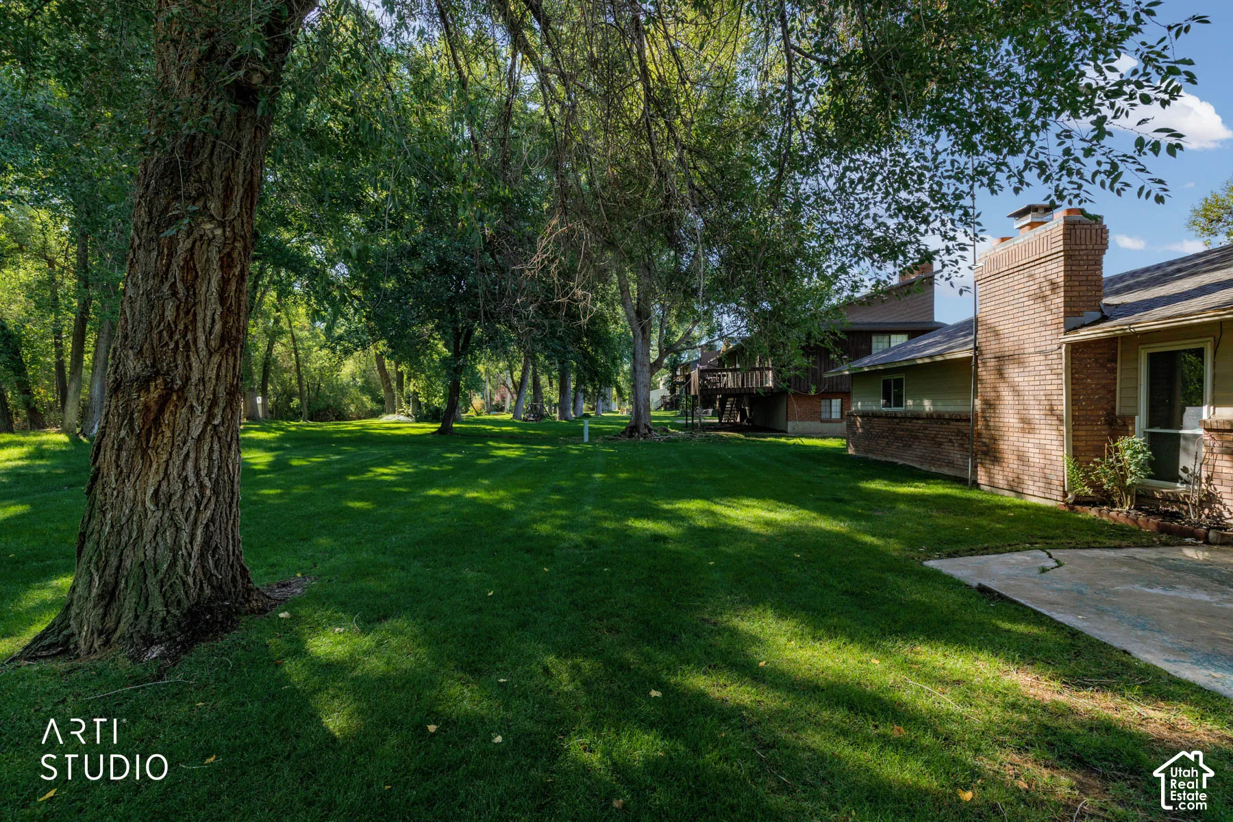Expansive green lawn with mature trees, a brick chimney, and a multi-level building with a wood deck