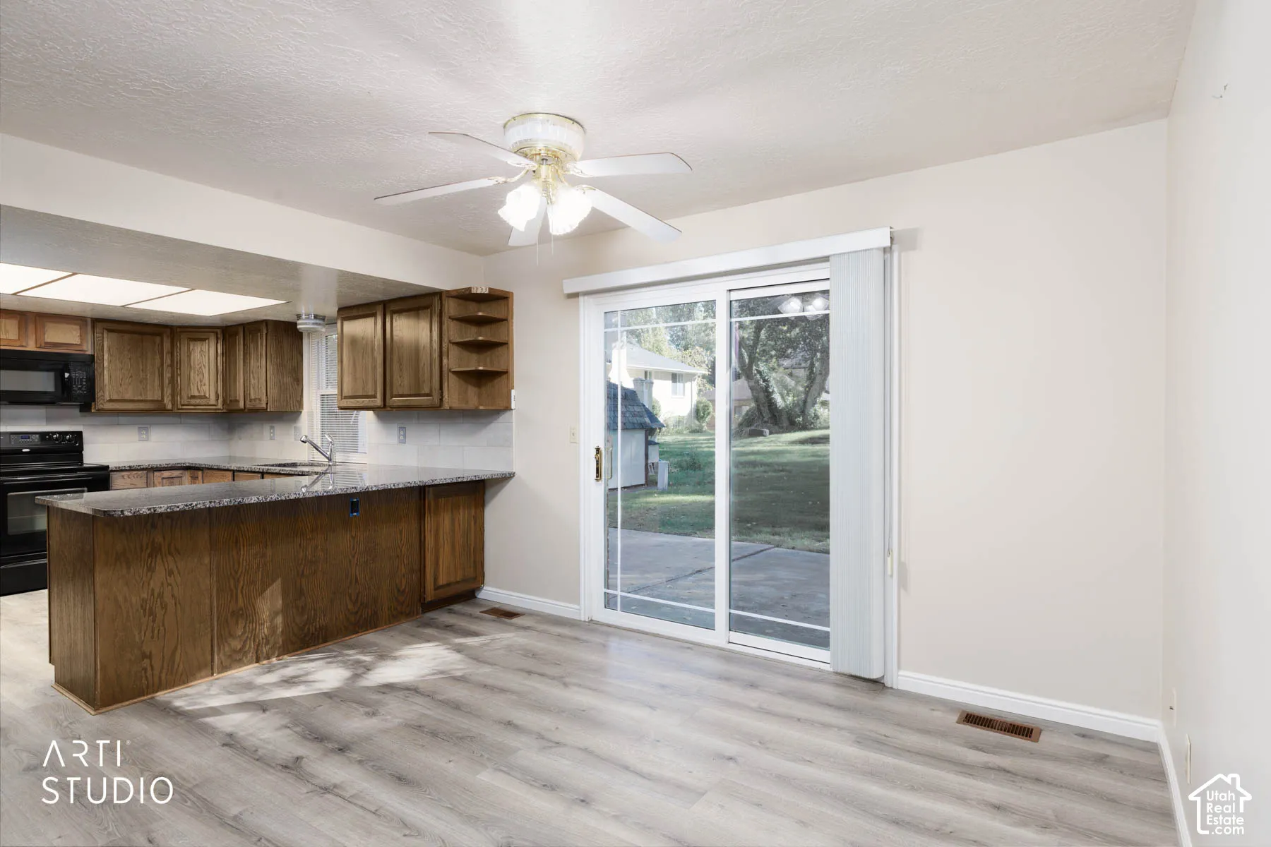 Wood-finish flooring, sliding glass door, kitchen island with seating, wood cabinetry, and a ceiling fan