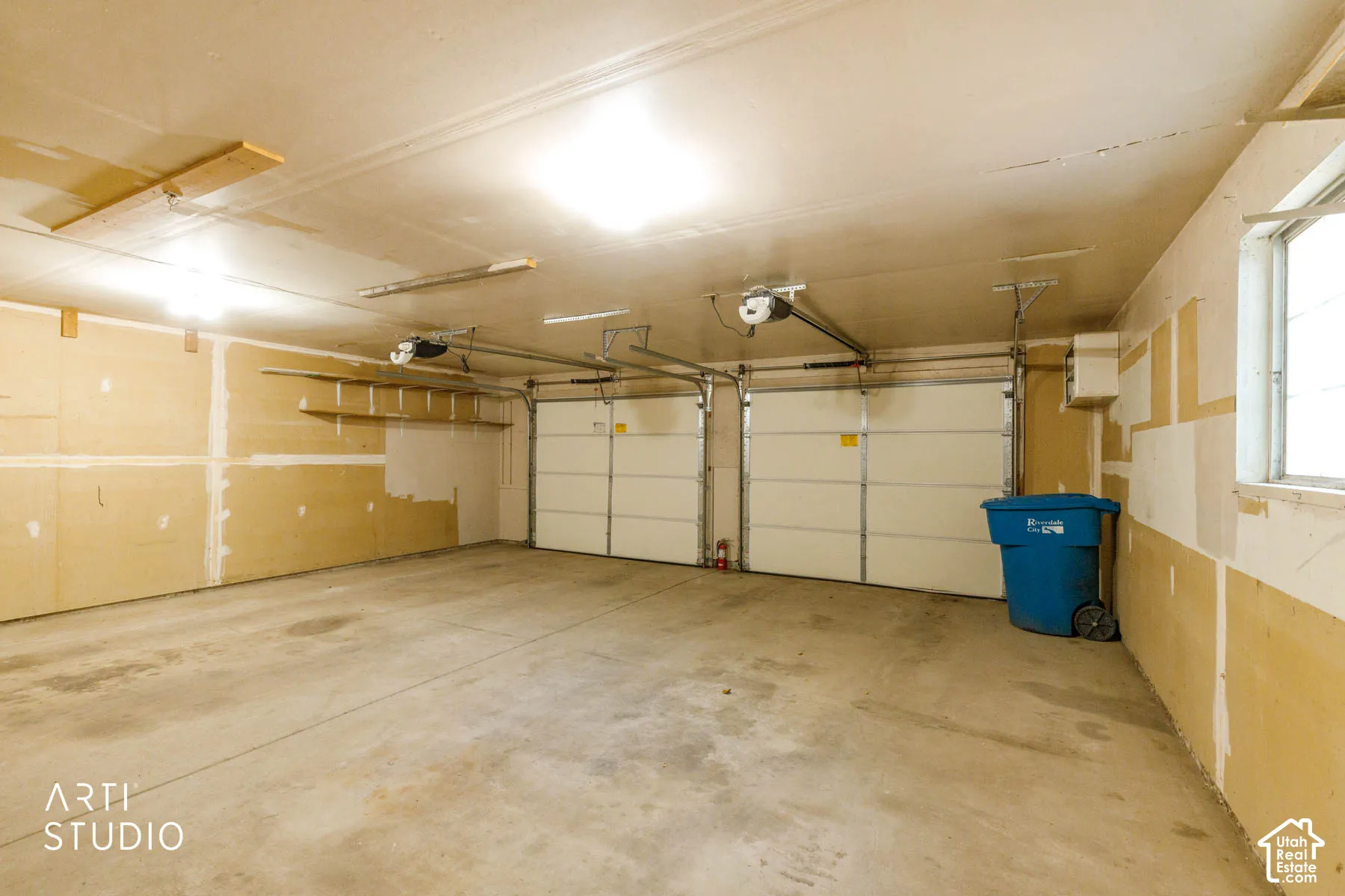 Two overhead garage doors with automatic openers, concrete flooring, and an exterior window