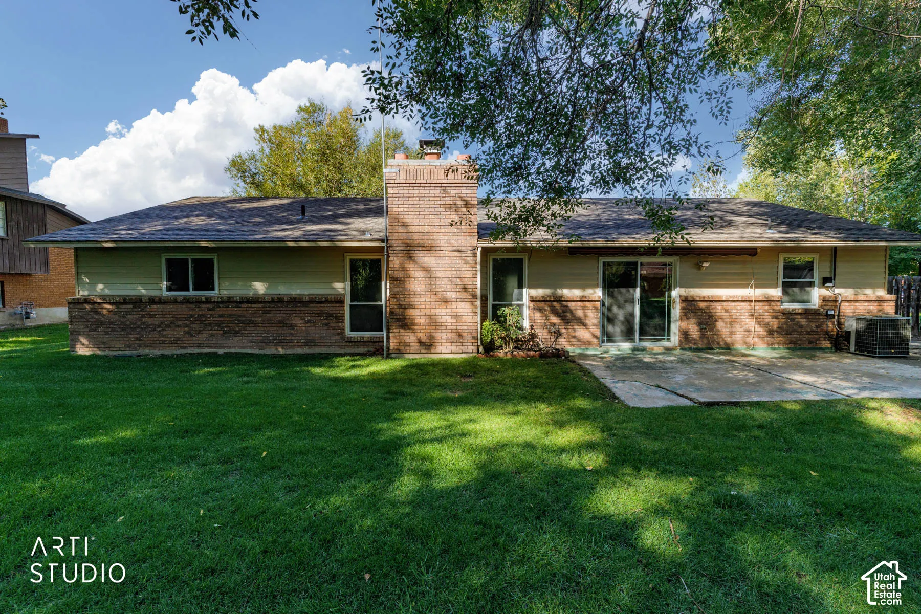 Expansive backyard featuring a manicured lawn, brick exterior accents, and a concrete patio