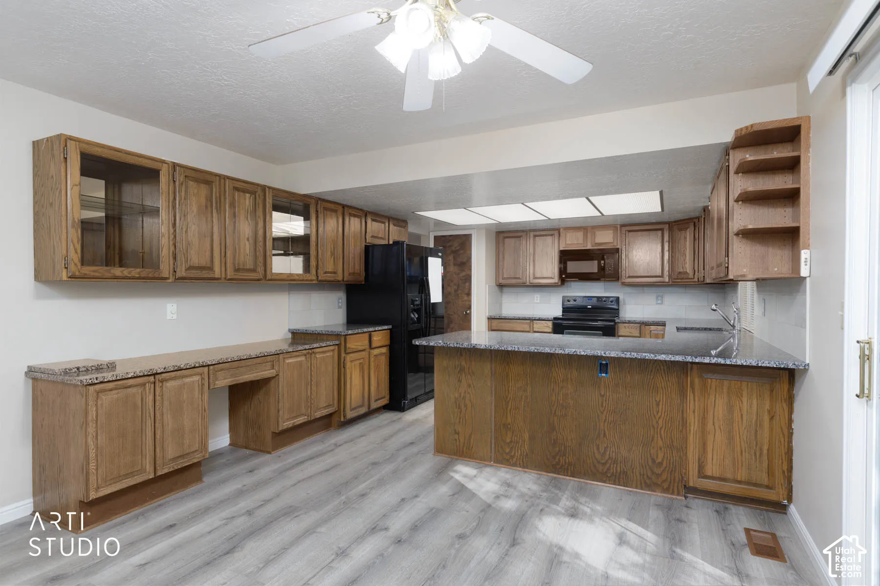 Spacious kitchen featuring a large island, wood-finish cabinetry, black appliances, light wood-finish flooring, and a ceiling fan with integrated lighting