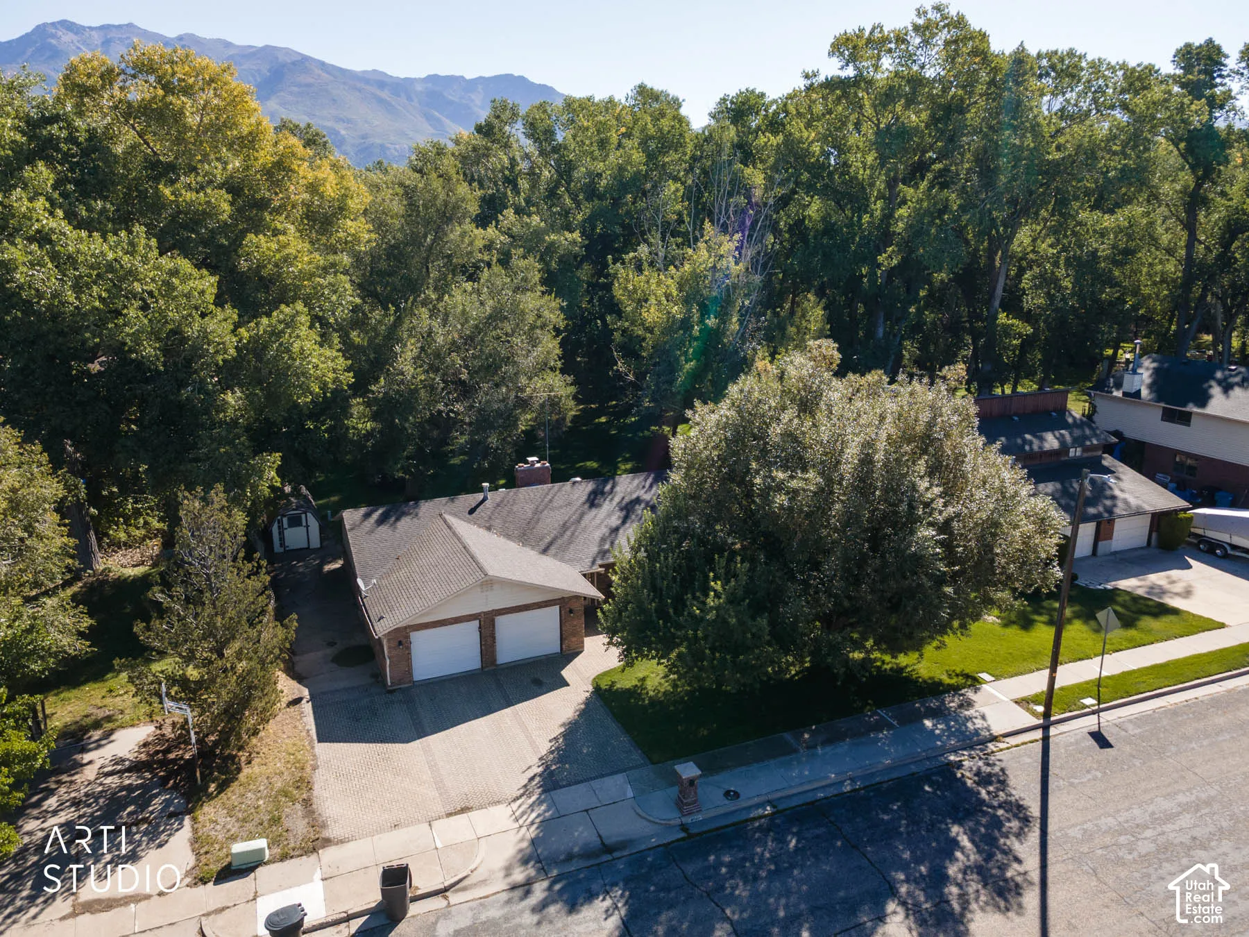 Brick exterior, two-car garage, paved driveway, mature trees, mountain backdrop