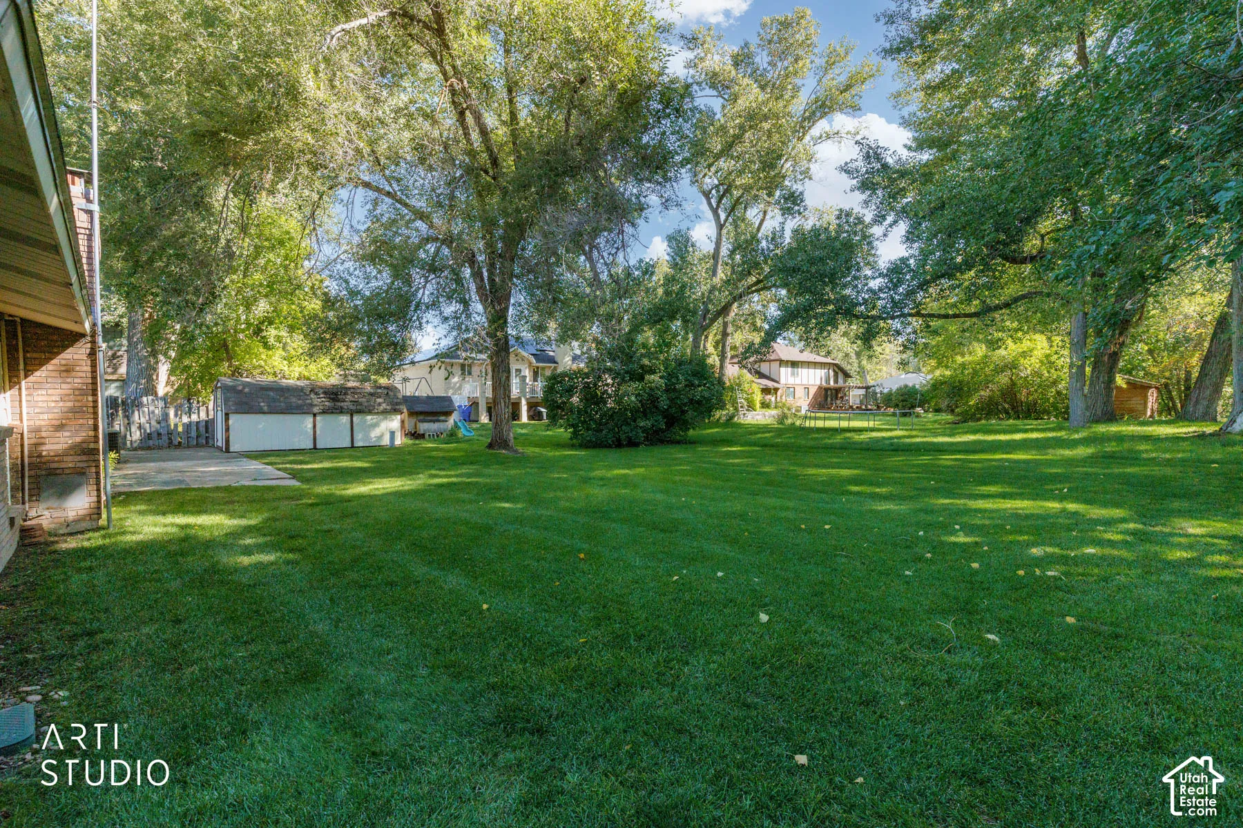 Expansive green lawn surrounded by mature trees, featuring a concrete patio and a detached garage with a white exterior