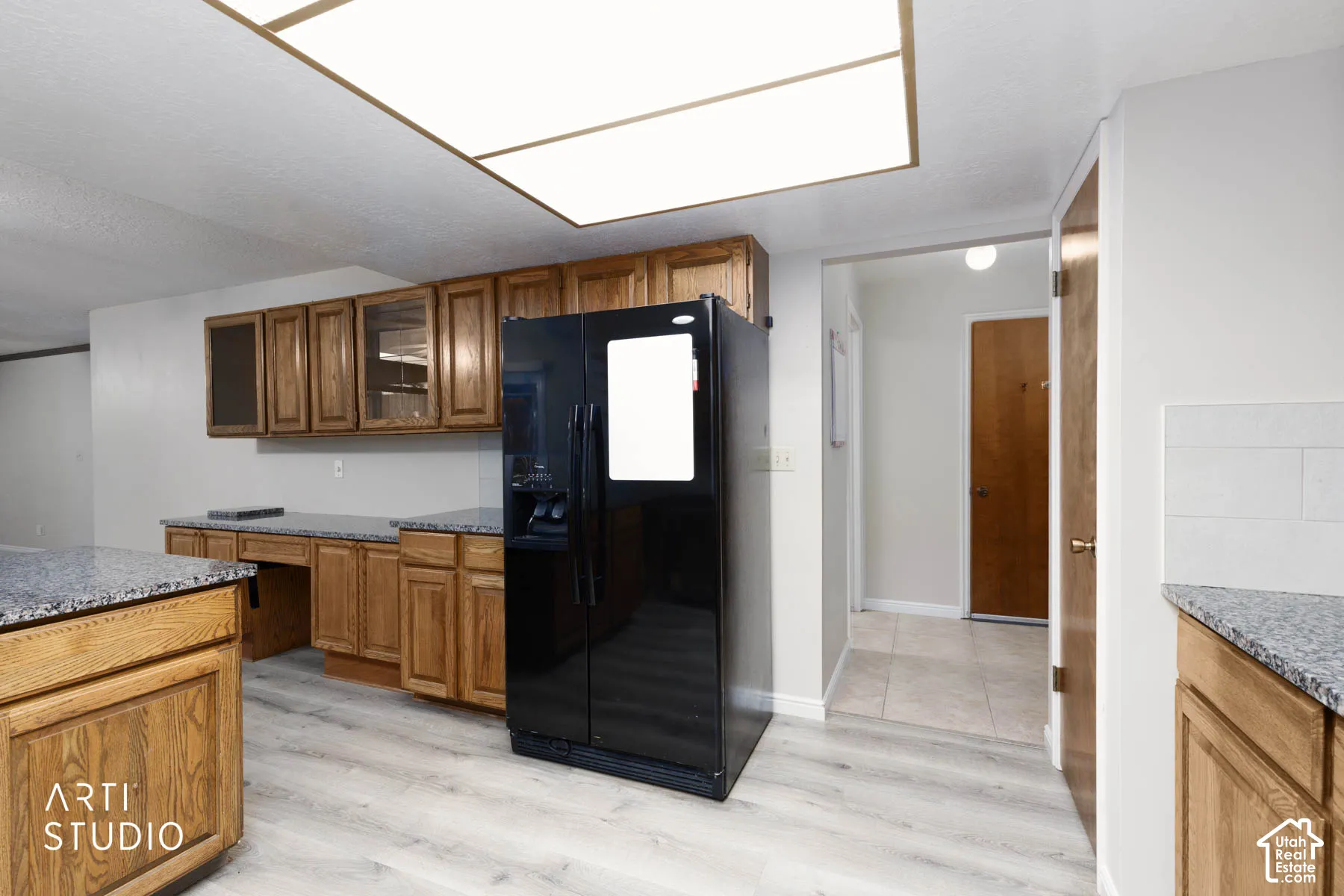 Kitchen featuring wood cabinetry, granite countertops, black refrigerator, and light wood-finish flooring