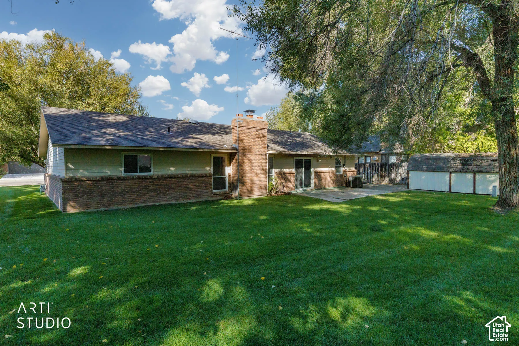 Expansive lawn with mature trees, brick veneer siding, a patio, and a detached shed