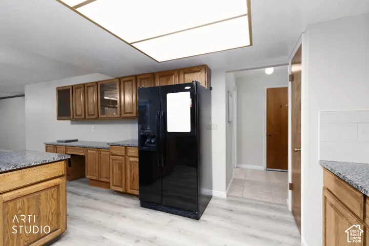 Kitchen featuring wood cabinetry, granite countertops, black refrigerator, and light wood-finish flooring