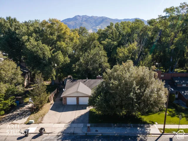 Mountain backdrop, mature trees, two-car garage, pitched roofline, paved driveway