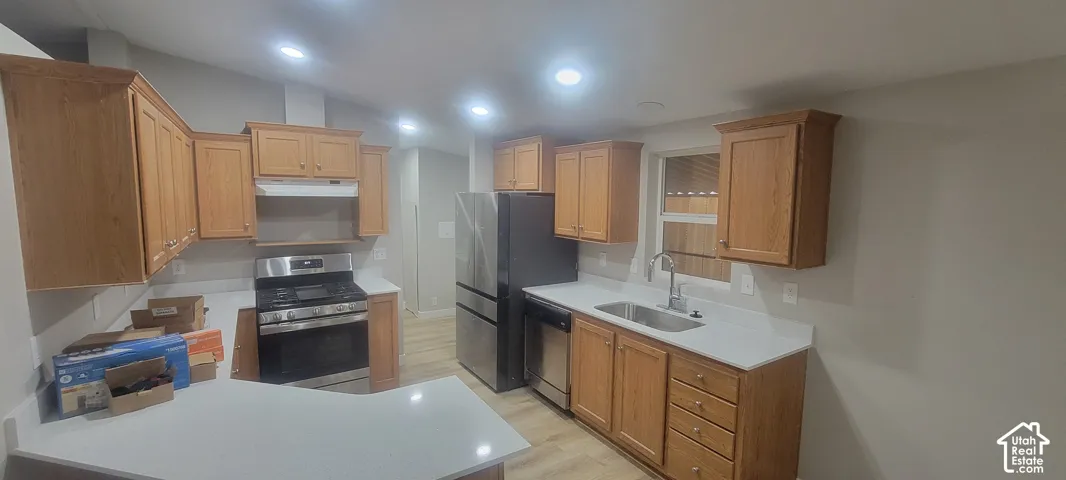 Light wood-finish cabinetry, stainless steel appliances, white countertops, recessed lighting, and wood-finish flooring