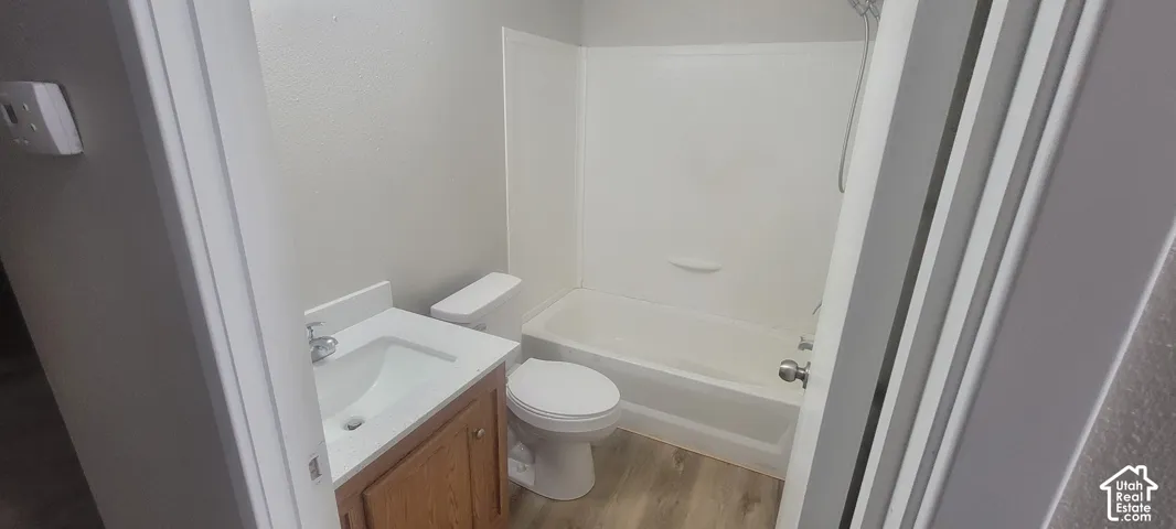 Bathroom featuring a vanity with an integrated sink, a toilet, a bathtub with a shower enclosure, and wood-finish flooring