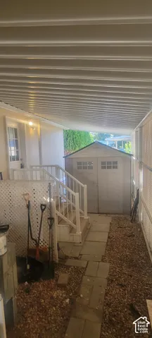 Covered outdoor area with a slatted ceiling, paved pathway, and exterior storage shed