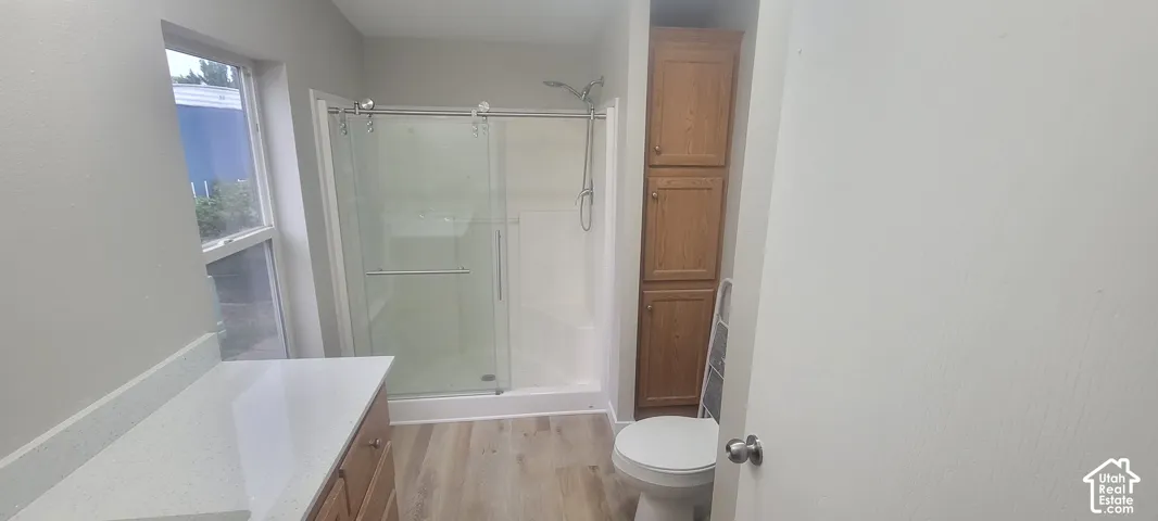 Spacious bathroom featuring a walk-in shower with sliding glass doors, a single vanity with a solid surface countertop, wood-finish flooring, and built-in wood cabinetry