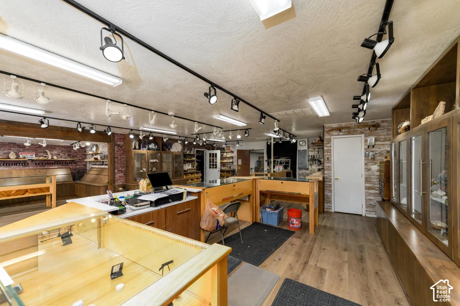 Wood-finish flooring, track lighting, exposed brick wall, white paneled door, and built-in display cabinetry